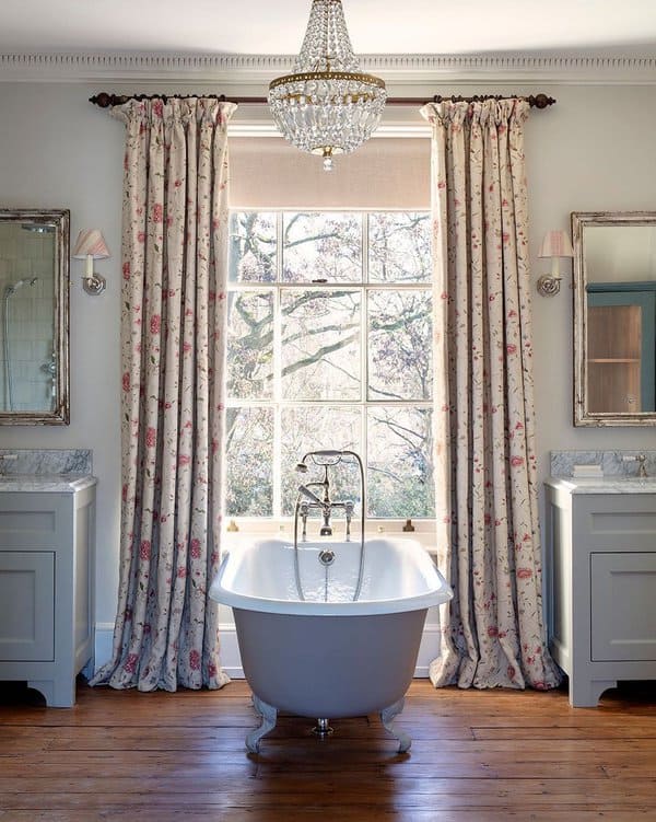 Vintage bathroom with floral curtains, freestanding bathtub, and crystal chandelier.