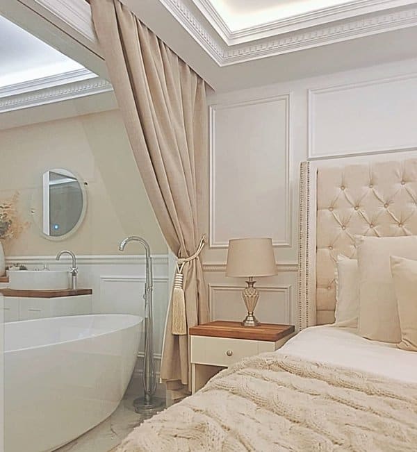 Cozy bedroom with beige curtains separating a freestanding bathtub and tufted headboard bed.