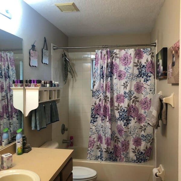 Small bathroom with floral shower curtain, beige countertop, and wall-mounted storage.