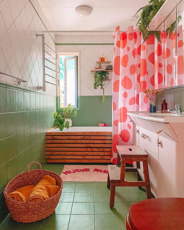 Vibrant bathroom with pink polka dot shower curtain, green tiles, and wooden tub paneling.