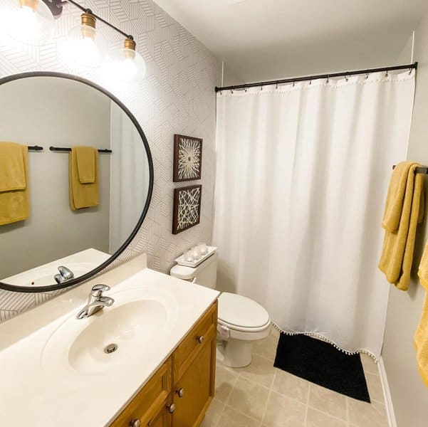 Modern bathroom with white shower curtain, round mirror, and yellow towel accents.