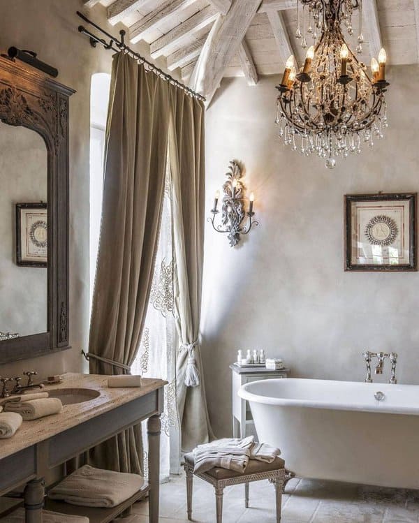 Rustic bathroom with elegant velvet curtains, freestanding tub, chandelier, and wooden accents.