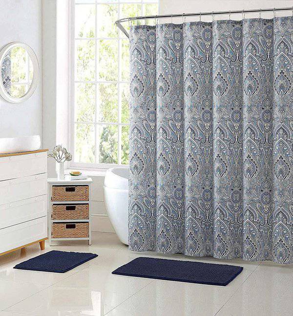 Light blue paisley patterned shower curtain in a bright bathroom with a white vanity and navy rugs.