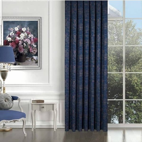 Dark blue patterned curtain in an elegant room with large windows, artwork, and a blue chair.