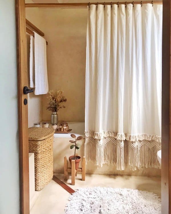 Boho-style bathroom with a white fringed shower curtain, wicker basket, and potted plant.