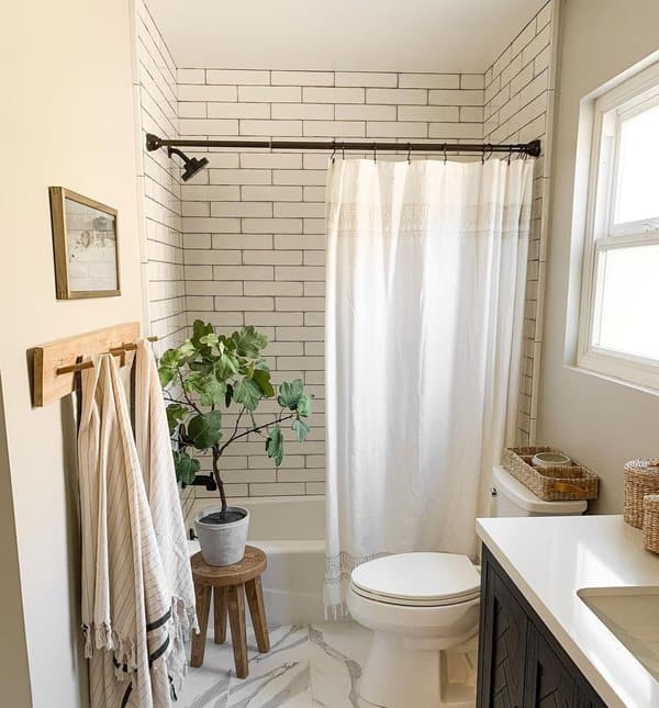 Small bathroom with a white shower curtain, subway tile, potted plant, and striped towels on hooks.