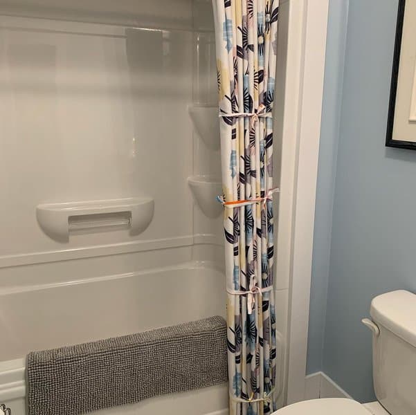 Small bathroom with a tropical print shower curtain, white bathtub, and gray towel on the tub edge.