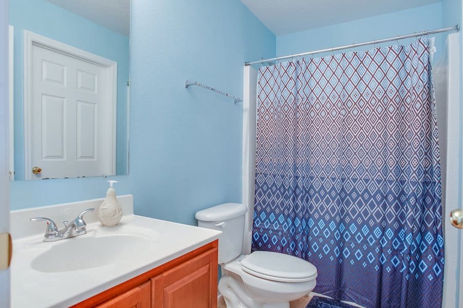 Small bathroom with a blue and purple ombre diamond-patterned shower curtain and light blue walls.