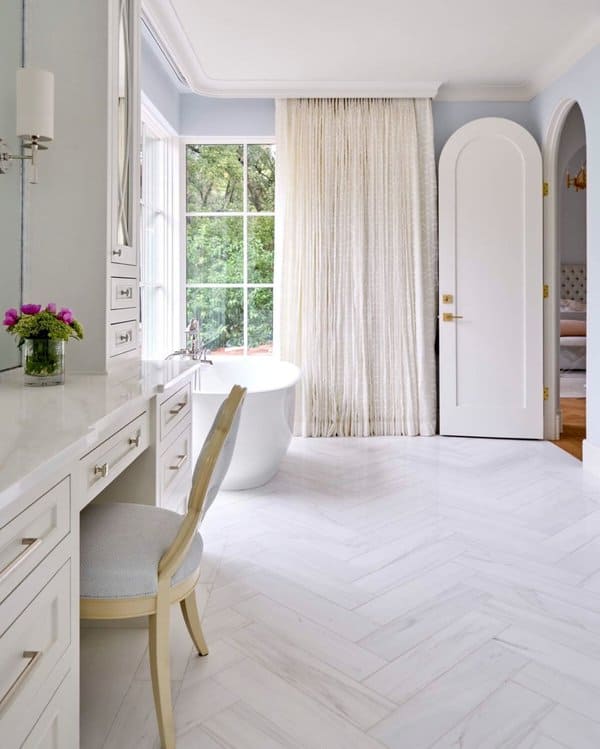 Luxurious bathroom with freestanding tub, large window, white curtains, and vanity area.