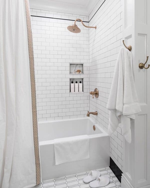 White subway-tile shower with brass fixtures, bathtub, and a hanging white curtain.