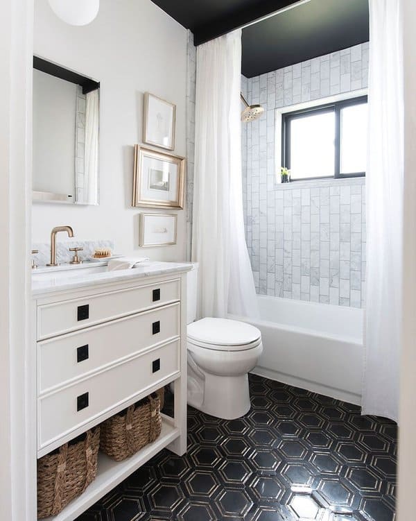 Small bathroom with marble tiles, white vanity, black hexagonal floor tiles, and white shower curtain.