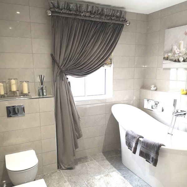 Modern bathroom with freestanding tub, glossy tiled walls, and grey draped curtains.