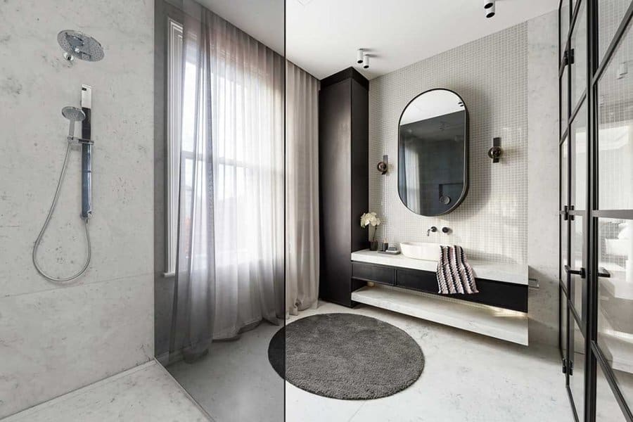 Sleek bathroom with glass shower, grey sheer curtains, oval mirror, and modern black vanity.