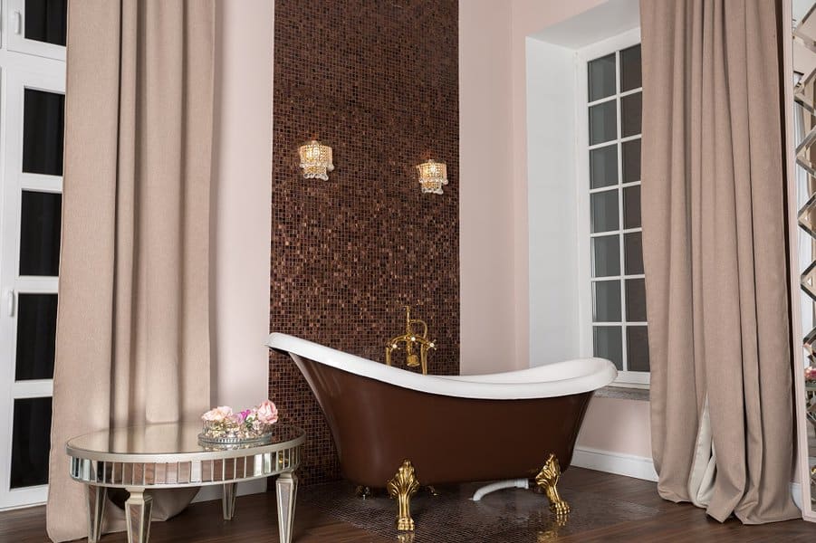 Luxurious bathroom with brown clawfoot tub, mosaic tile accent wall, and beige curtains.