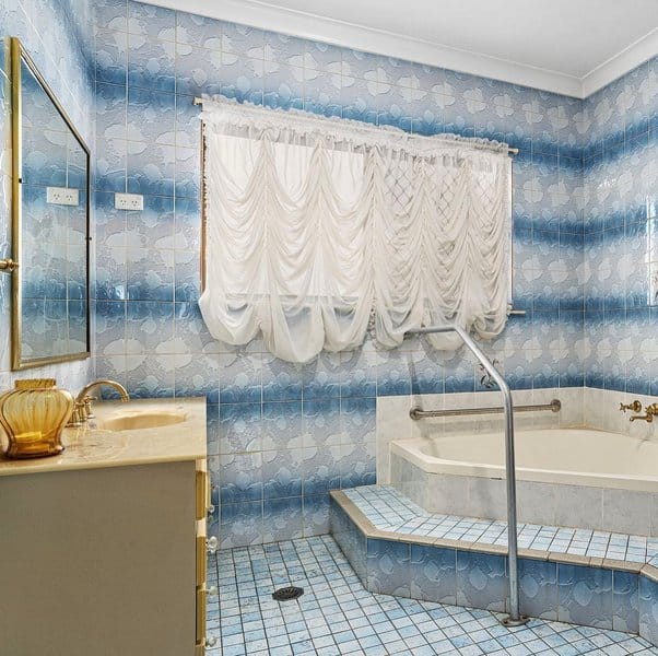 Retro-style bathroom with blue tiled walls, draped white curtains, and a step-up bathtub.