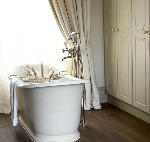 Classic bathroom with freestanding tub, light beige curtains, and dark wood flooring.