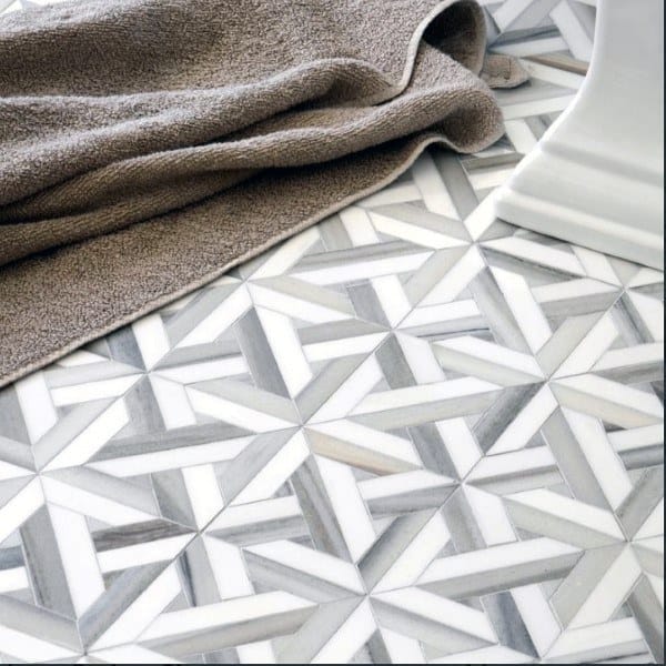 Bathroom with intricate gray and white geometric mosaic floor tiles and a textured towel nearby.