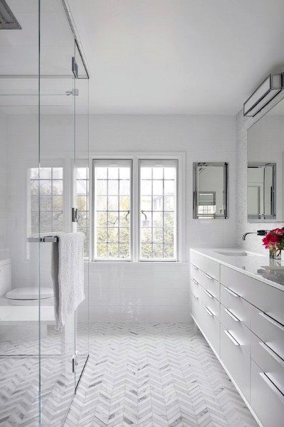 Bright bathroom with white herringbone floor tiles, glass shower, and large windows.