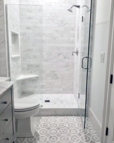 Small white bathroom with glass shower, marble subway wall tiles, and hexagonal floor tiles.