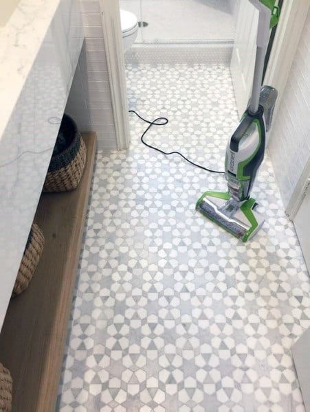 Bathroom with white and gray mosaic patterned floor tiles, wooden shelves, and white tiled walls.