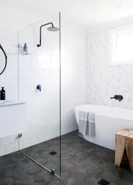 Modern bathroom with glass shower, white bathtub, and hexagonal dark gray floor tiles.