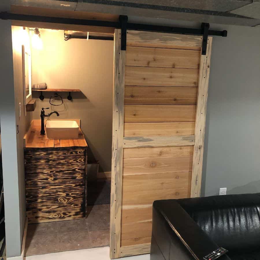 Basement bathroom with rustic wooden sliding door and wood vanity with vessel sink.