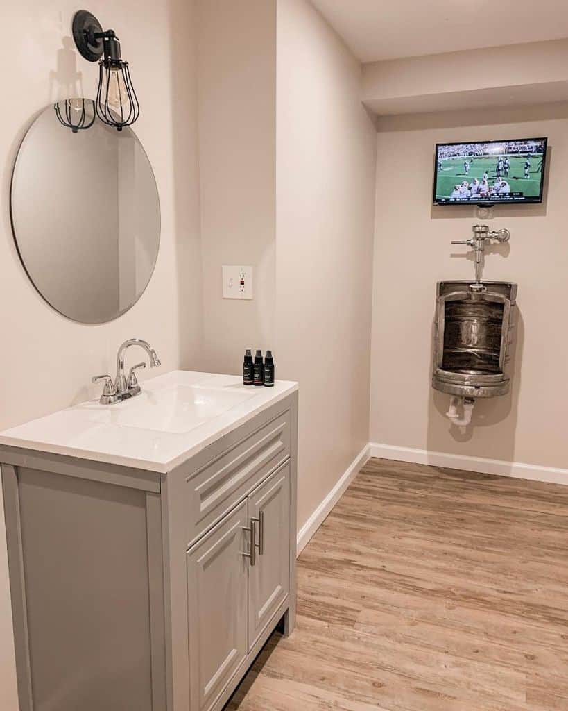 Modern bathroom with urinal, wall-mounted TV, and single vanity with round mirror.