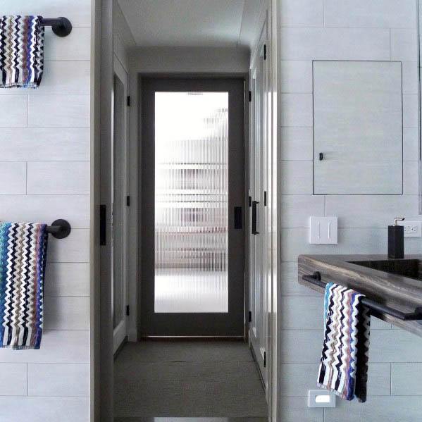 Modern bathroom with frosted glass pocket door, sleek black fixtures, and colorful chevron-patterned towels