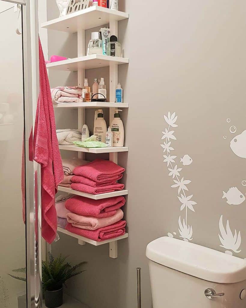 Tall white bathroom shelf with towels, toiletries, and decor next to shower and toilet.