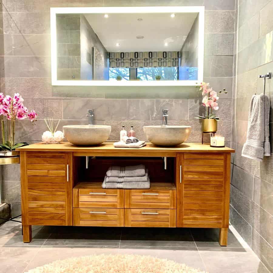 Modern bathroom with wooden double vanity, stone vessel sinks, and large illuminated mirror.