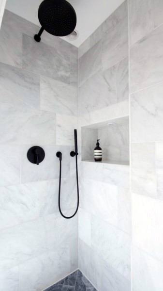 Modern marble shower with black fixtures, rainfall showerhead, and built-in niche.