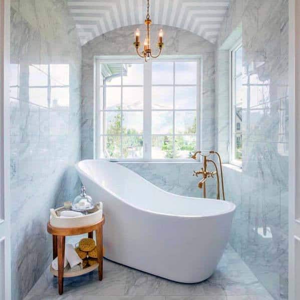 Elegant bathroom with a freestanding white tub, a small round table, large windows, and a chandelier