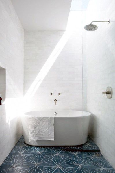 Freestanding tub with white subway tile wall and blue patterned floor in bright bathroom.