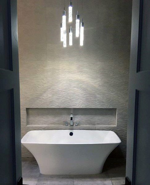 Freestanding white bathtub with textured wall tiles and modern pendant lighting.