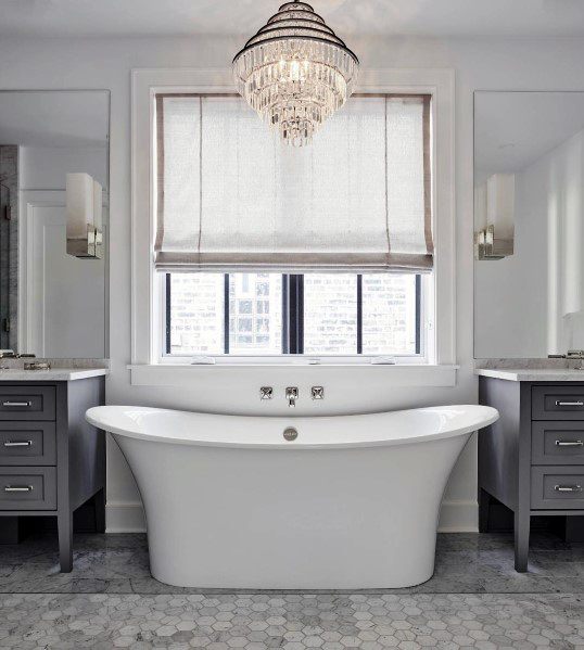 Large freestanding bathtub with chandelier and double vanities in a bright bathroom.