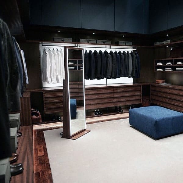 Spacious walk-in closet with a full-length mirror, clothes on racks, and a large blue ottoman in the center