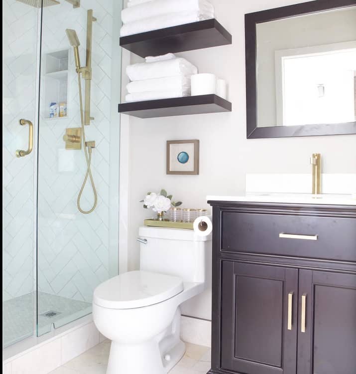 Modern bathroom with glass shower, black vanity, and floating shelves filled with towels above the toilet