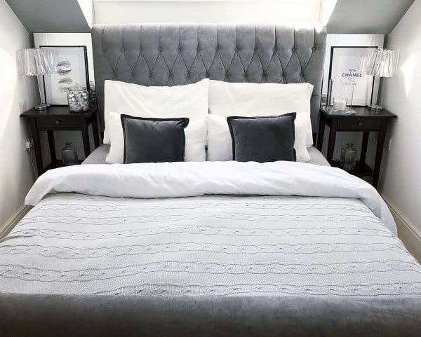 Elegant bedroom with a grey tufted headboard, white and grey pillows, side tables, and framed art