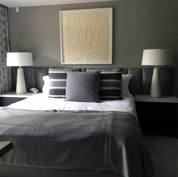 Modern gray bedroom with striped pillows, textured lamps, and leaf-inspired wall art.