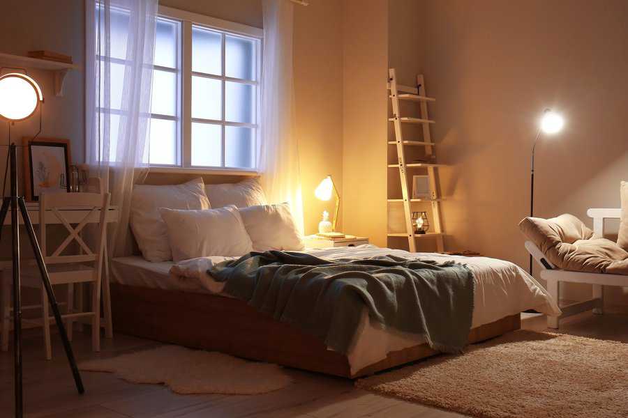 Cozy bedroom with warm lighting, layered bedding, and a ladder-style shelf by the wall.