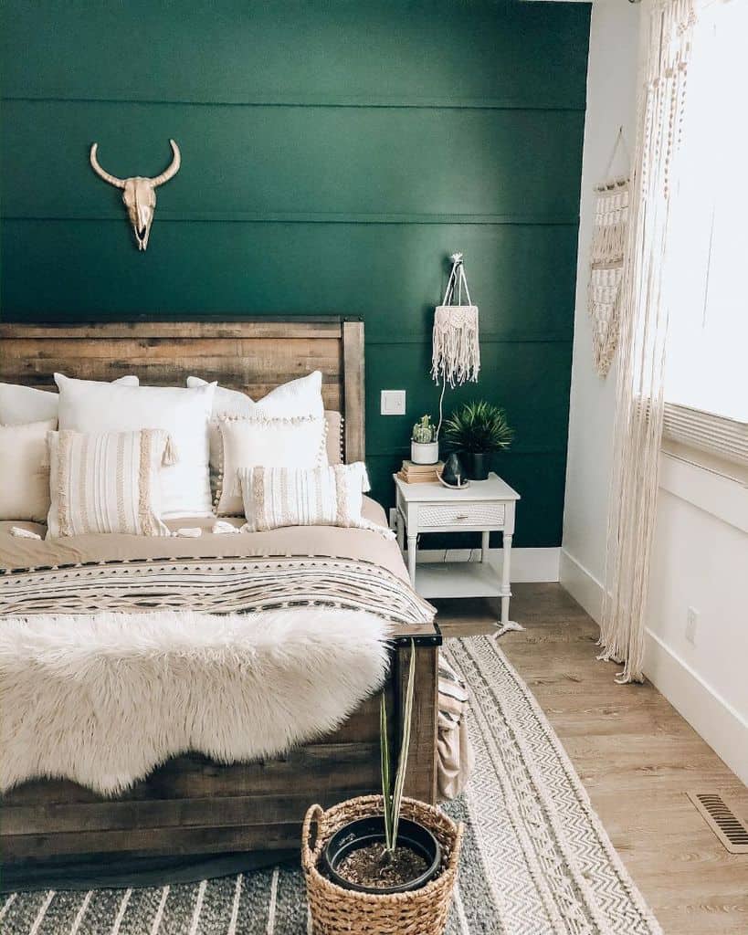 Farmhouse-style bedroom with green accent wall, rustic wood bed, macrame wall decor, and cozy neutral bedding.