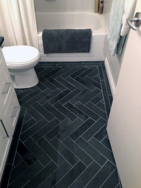 Bathroom with dark herringbone floor tiles, white fixtures, and a bathtub with a gray towel.