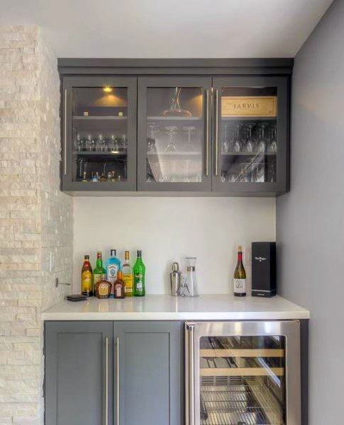 Modern mini bar with gray cabinets, glassware storage, beverage fridge, and white quartz countertop.