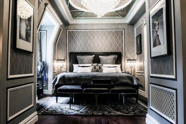 Elegant bedroom with chandelier, patterned walls, and luxurious black and gray decor.