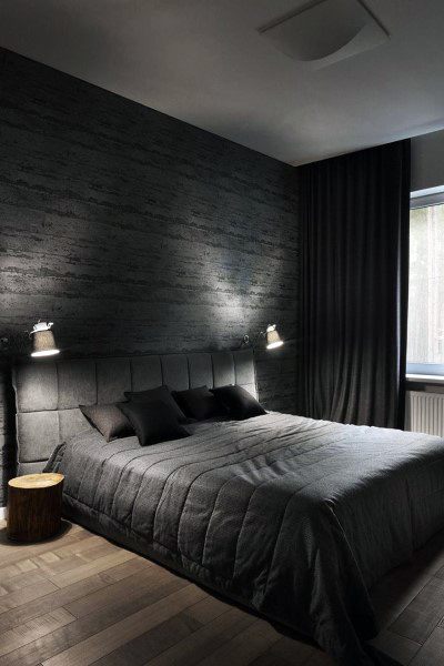 Dark bedroom with black bedding, textured wall, and wood flooring.