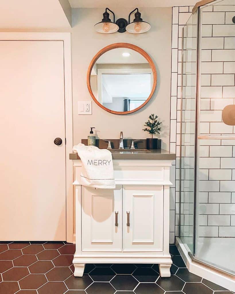 Simple black and white bathroom design with round mirror, subway tiles, and hexagon floor tiles.