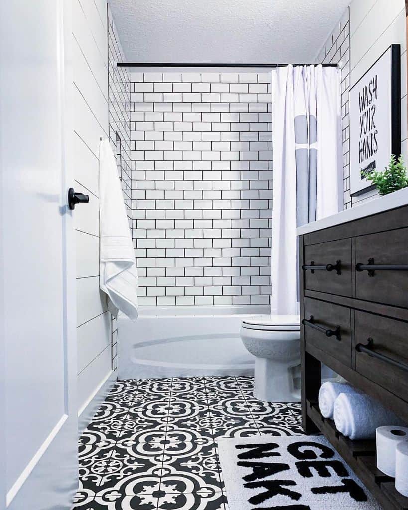 Simple black and white bathroom with a tub, subway tile walls, and decorative floor tiles.