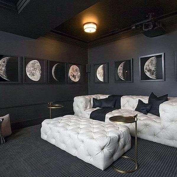 Chic mancave with dark walls, white tufted sectional, moon phase artwork, and modern lighting.