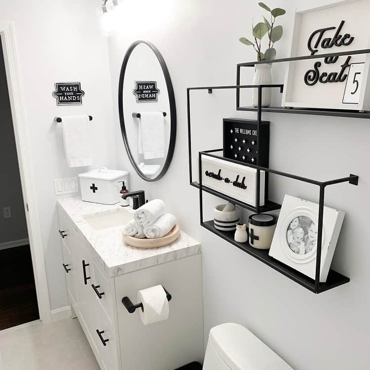 Black and white bathroom with steel shelves, black accent mirror, and minimalist decor.