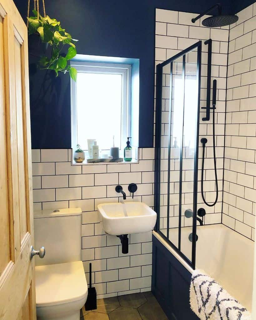 Modern black and white bathroom with subway tiles, navy accents, and hanging greenery.